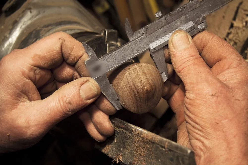 Handen van een vakman meten een gedraaid stuk hout met een schuifmaat