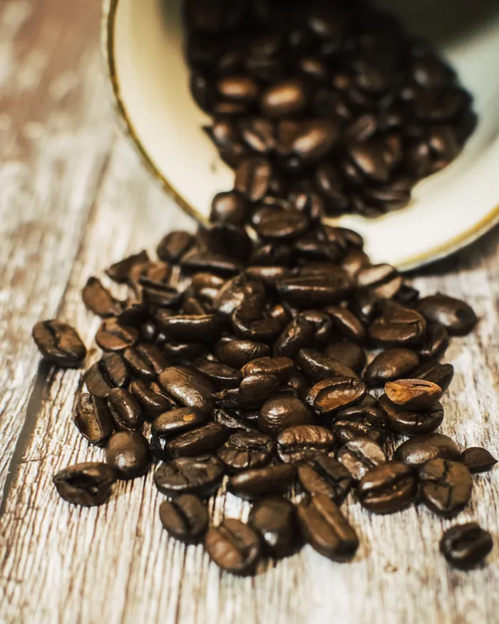 Koffiebonen die uit een kom over een houten tafel rollen